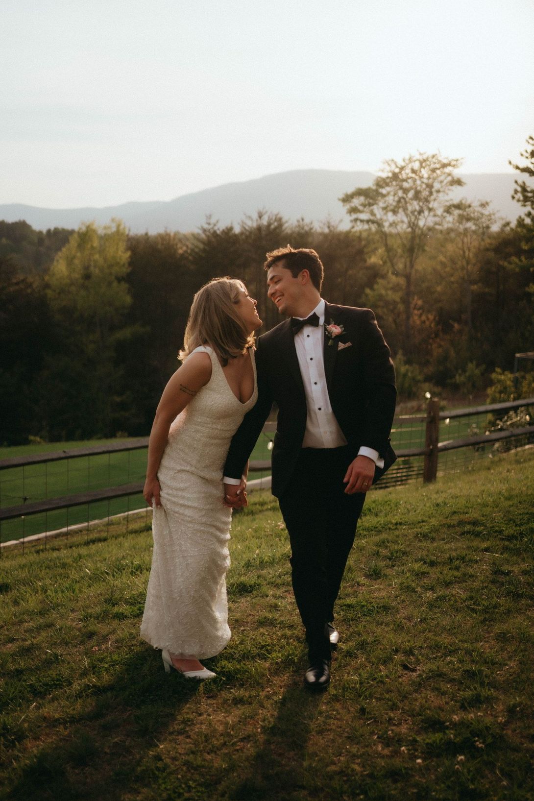 Couple walking hand in hand, laughing joyfully on the scenic ridge near Hilltop House at Serenity Ridge with mountain views.