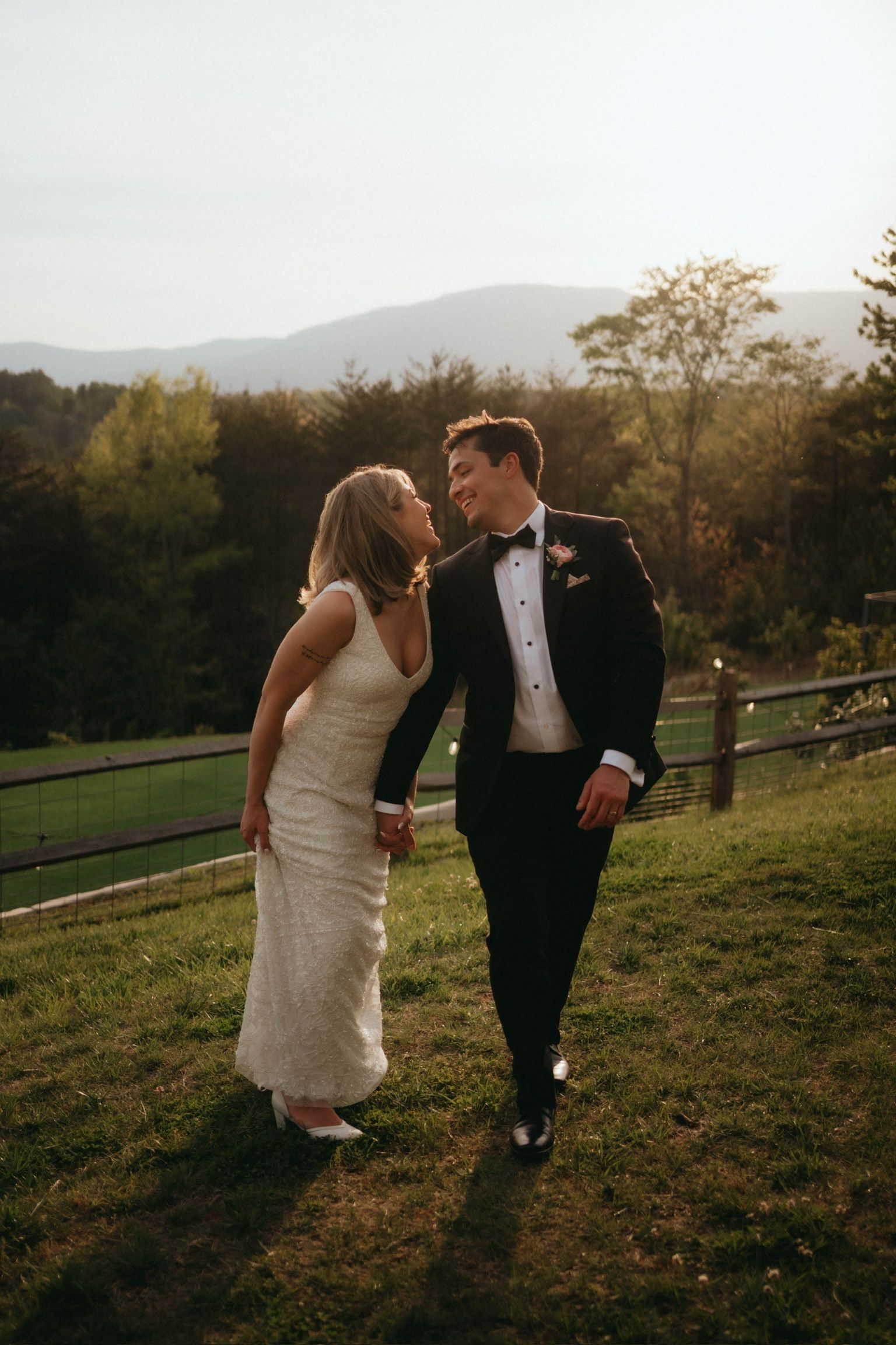 Couple walking hand in hand, laughing joyfully on the scenic ridge near Hilltop House at Serenity Ridge with mountain views.