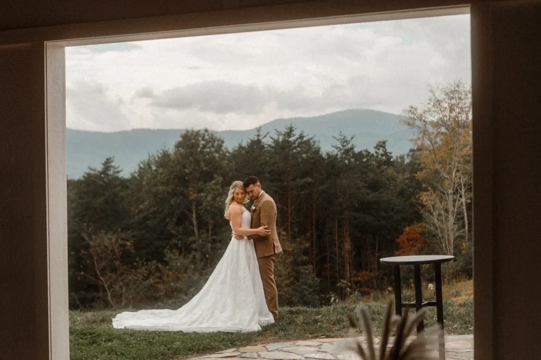 Couple embracing on ceremony lawn with panoramic Blue Ridge Mountain views in WNC at Serenity Ridge wedding venue.