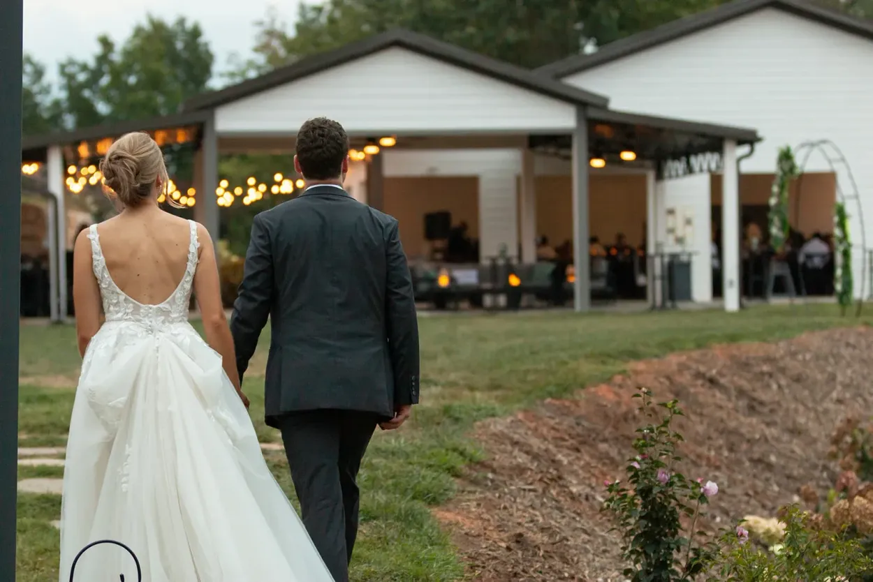 Newlyweds walk hand in hand toward their mountain reception at Serenity Ridge’s outdoor event pavilion.