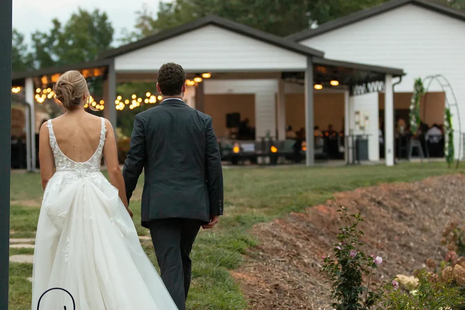 Newlyweds walk hand in hand toward their mountain reception at Serenity Ridge’s outdoor event pavilion.