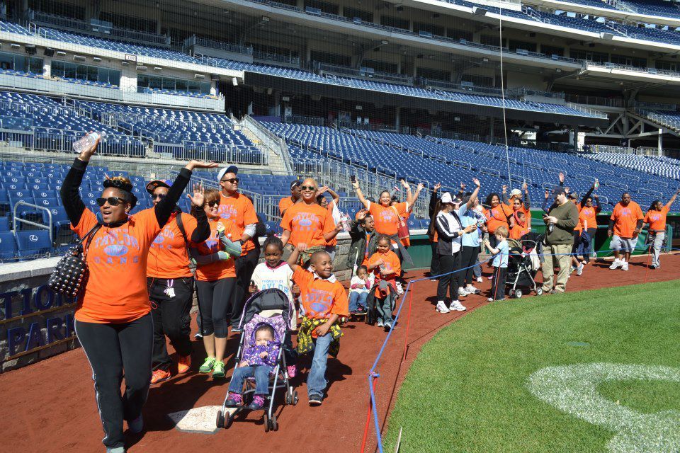 A group of people in orange shirts are walking on a baseball field