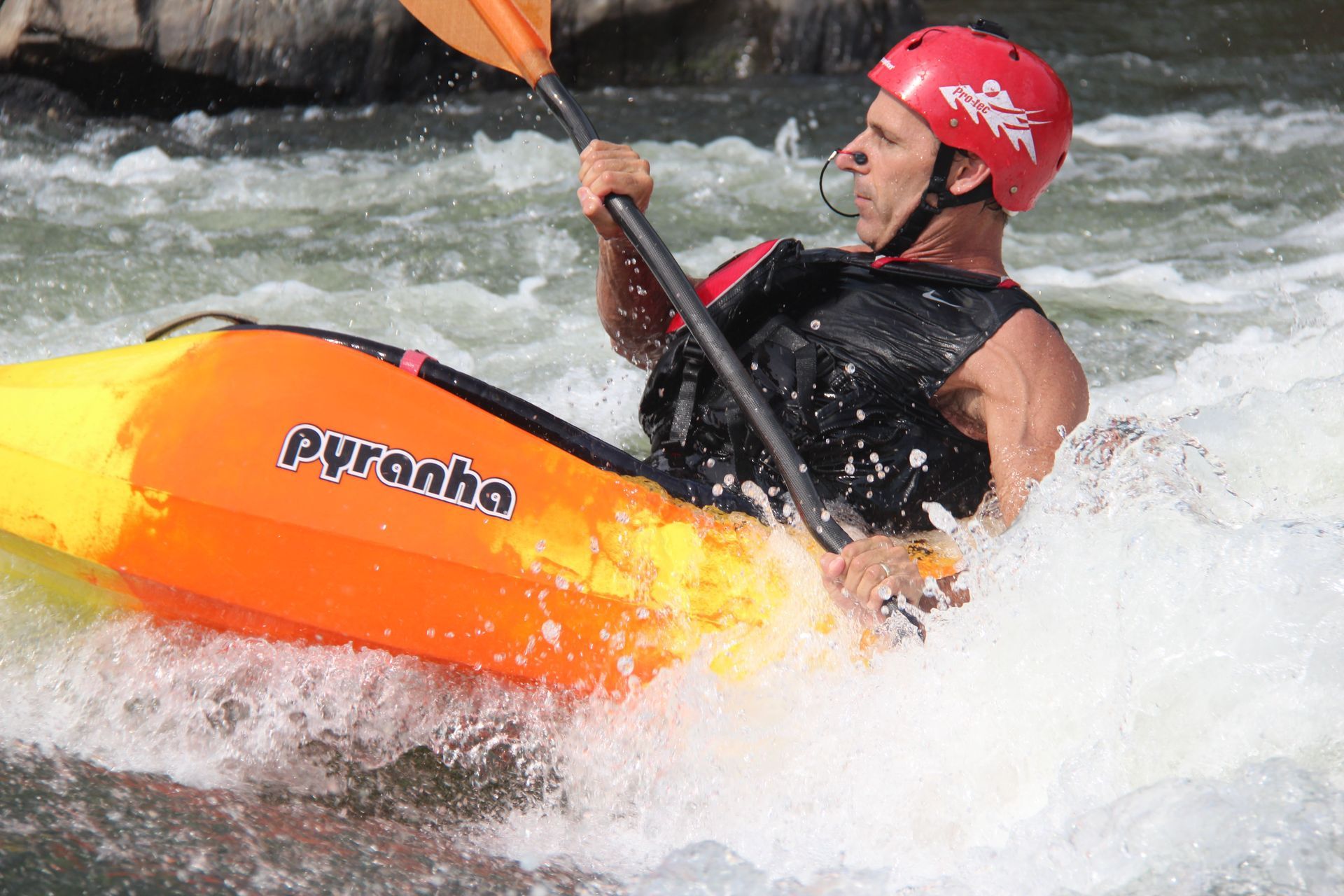 A man in a red helmet is paddling an orange kayak