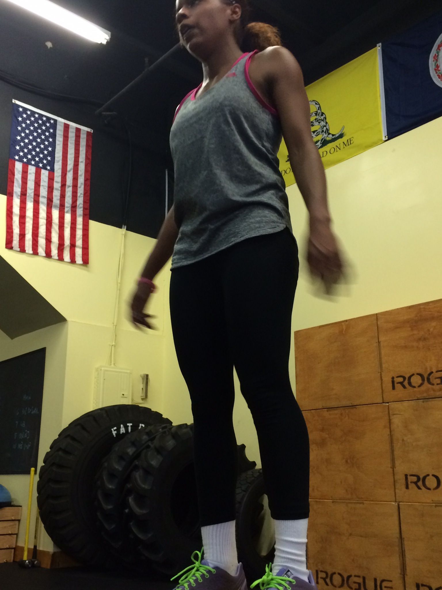 A woman is jumping over a tire in a gym