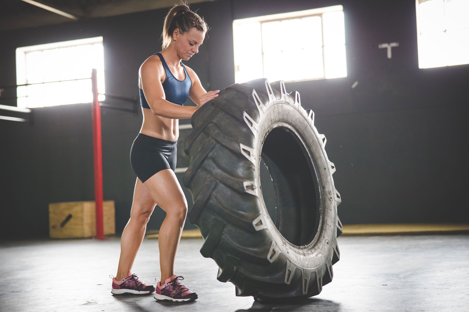 A woman is lifting a large tire in a gym