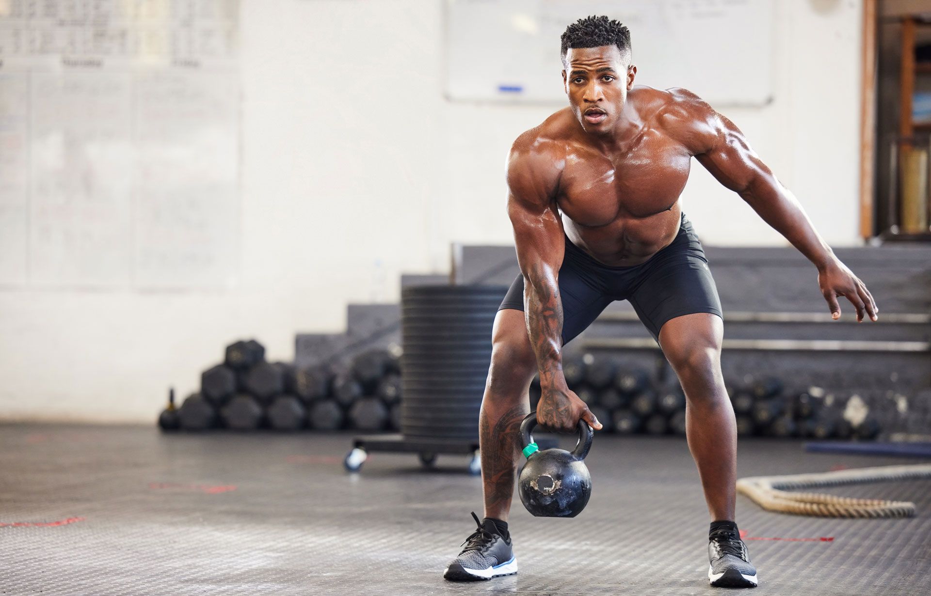 A shirtless man is lifting a kettlebell in a gym