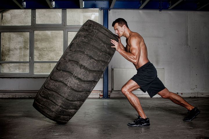 A man is pushing a large tire in a gym