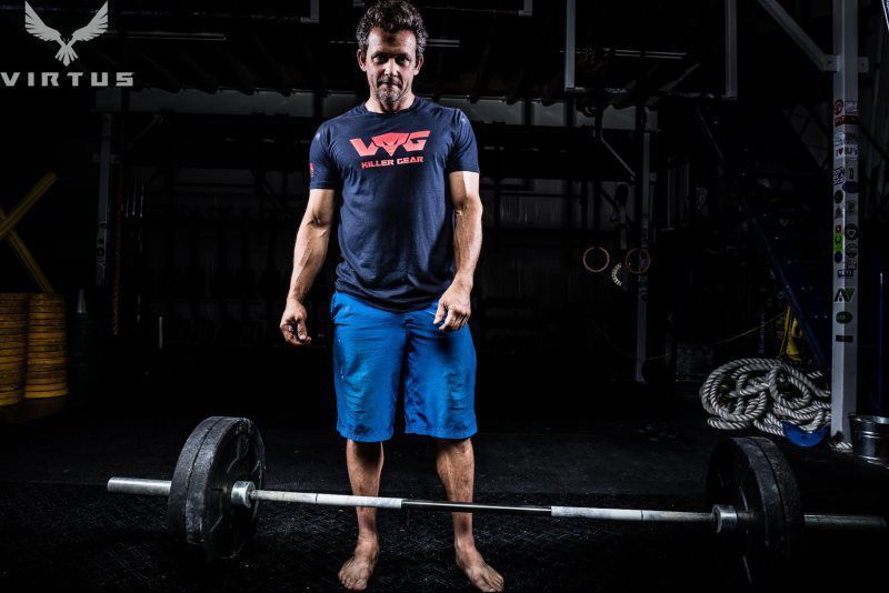 A man is standing next to a barbell in a gym