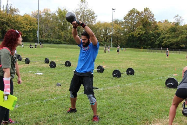 A man is lifting a kettlebell over his head in a field