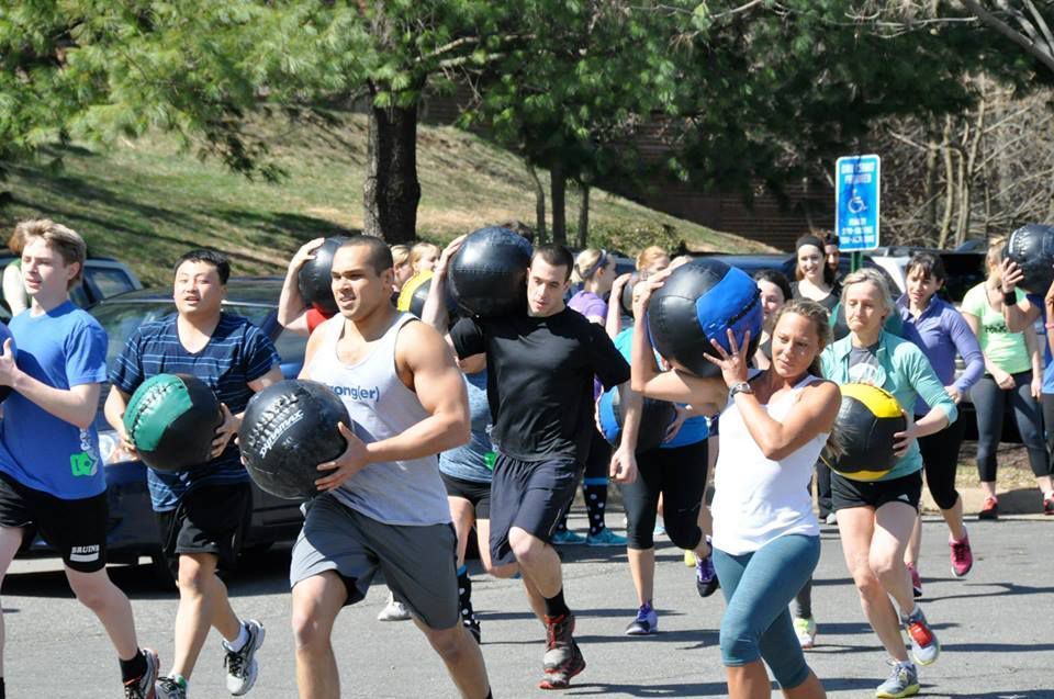 A group of people are running with medicine balls in a parking lot