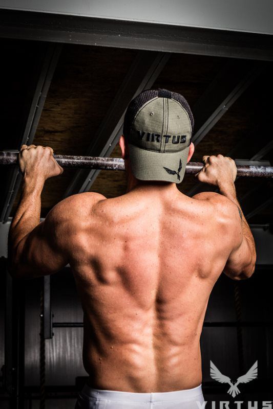 A shirtless man is doing pull ups on a bar in a gym