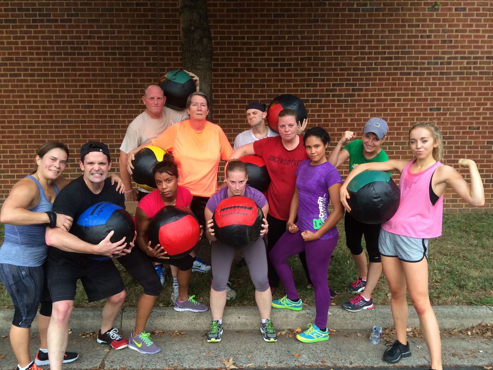A group of people are posing for a picture with medicine balls in front of a brick wall