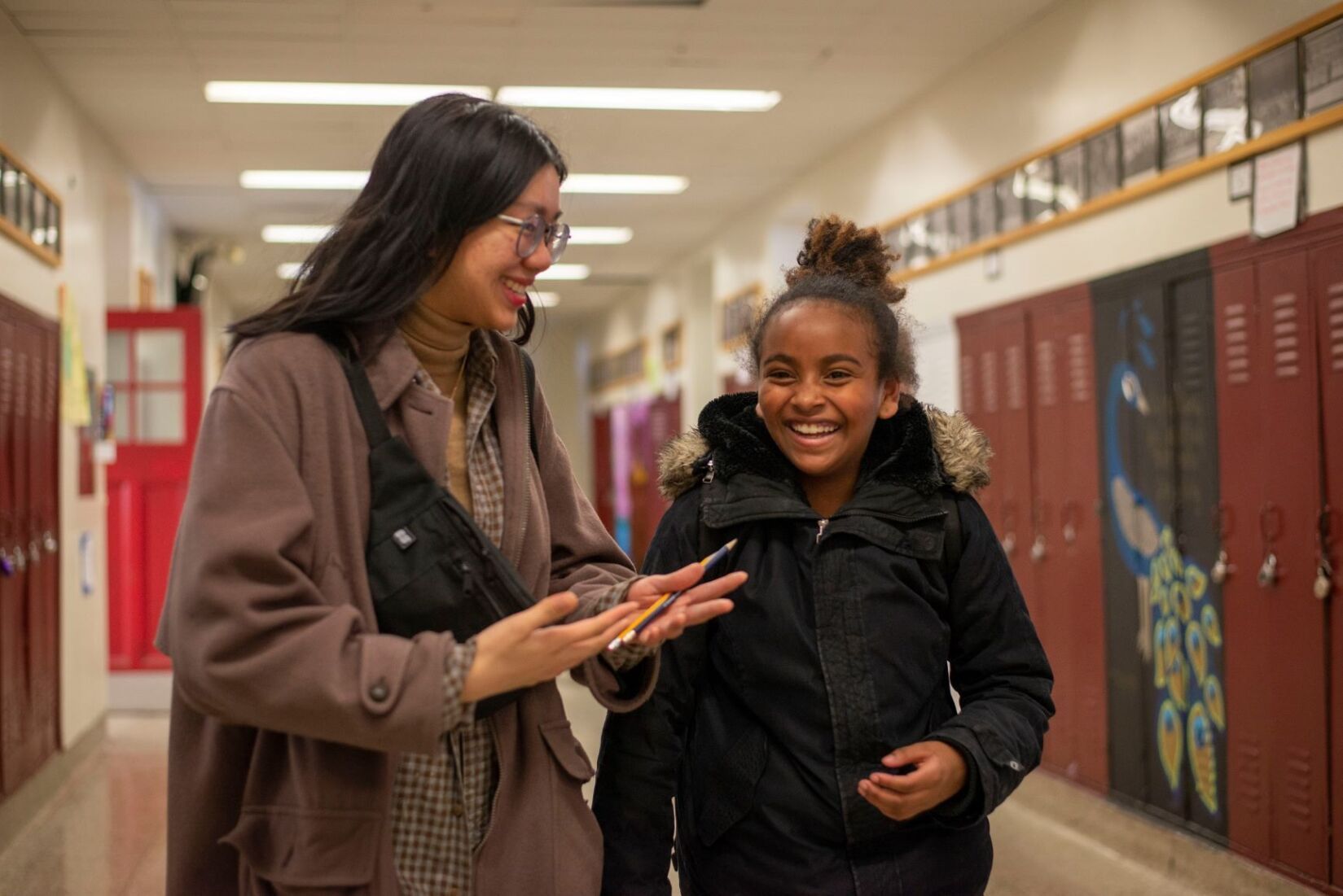 Two women are walking down a hallway and talking to each other.