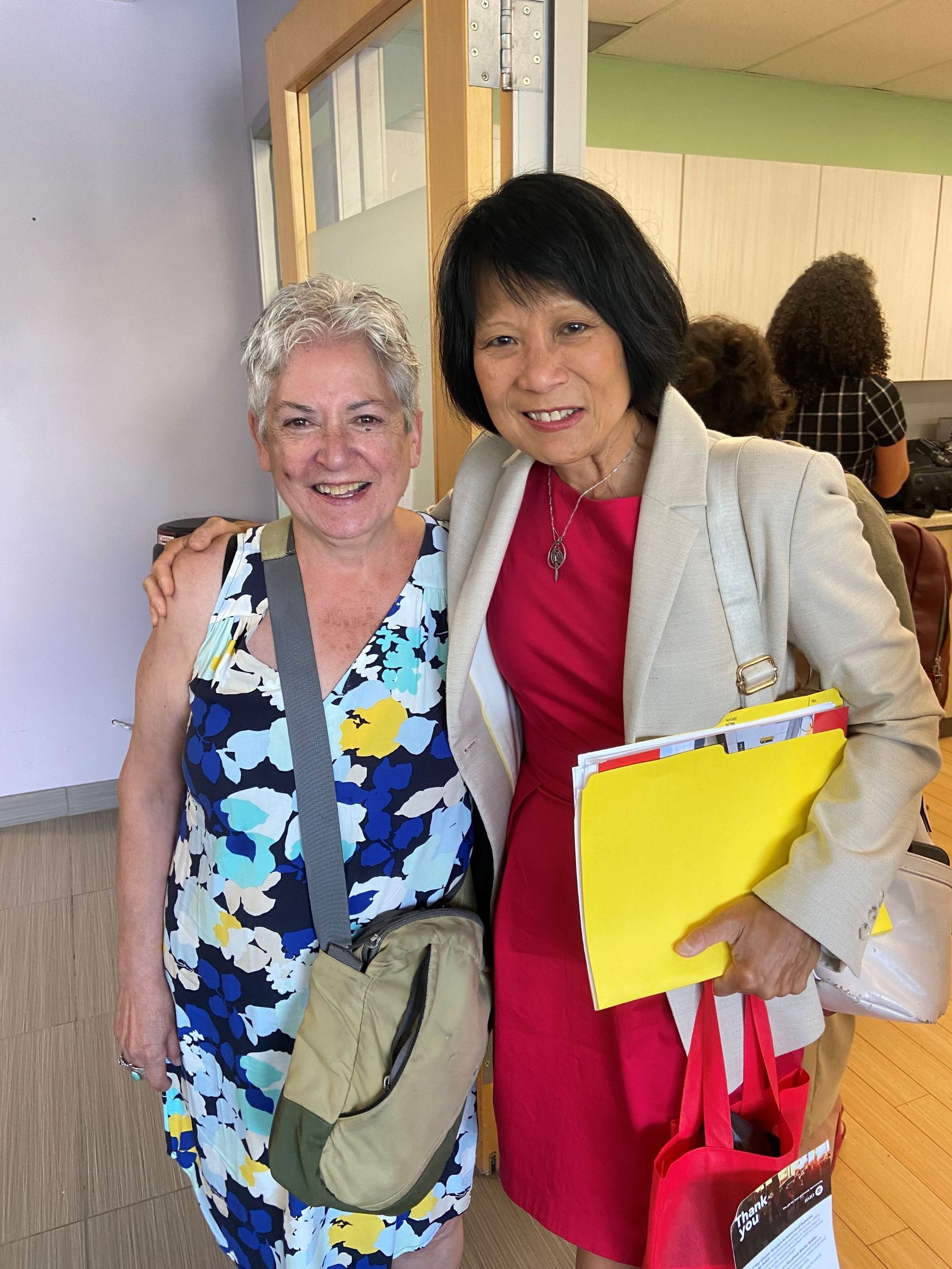 two women are posing for a picture and one is holding a yellow folder