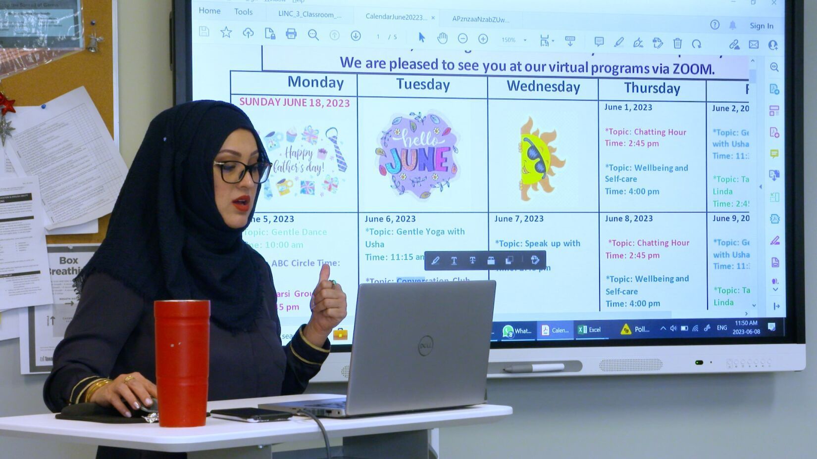 A woman in a hijab is sitting at a desk in front of a large screen.