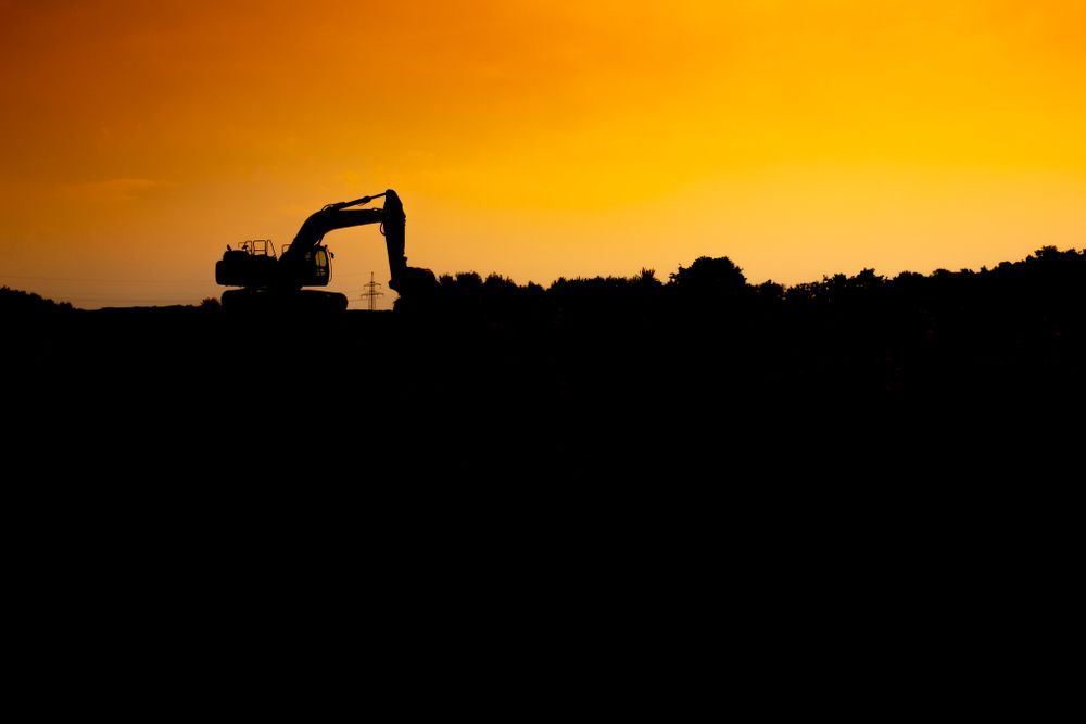 Silhouette of an excavator against an orange sunset; construction site.