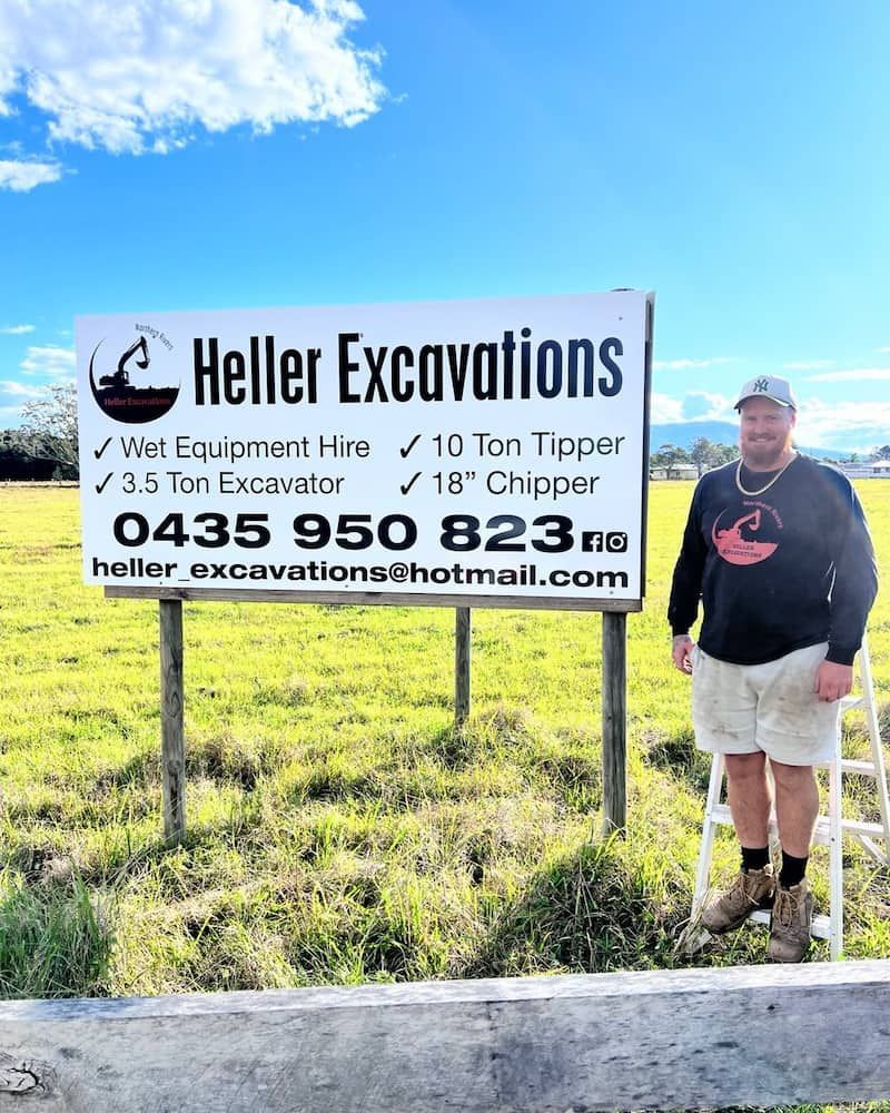 Man Stands Next to a Heller Excavations Sign in a Field — Heller Excavation & Tree Services in Mullumbimby, NSW