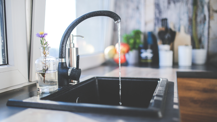 Modern kitchen sink with black faucet dripping water, countertop and blurred background