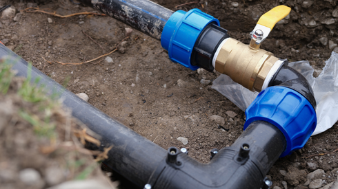 Blue pipe fittings and a brass valve connected to underground irrigation pipes in a dirt trench.