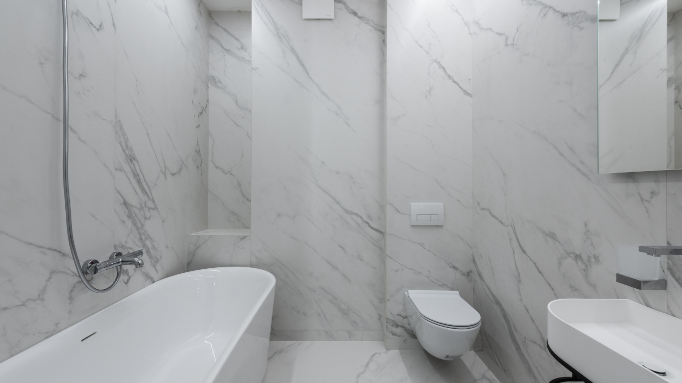 Modern bathroom with white marble walls, a freestanding tub, toilet, and sink