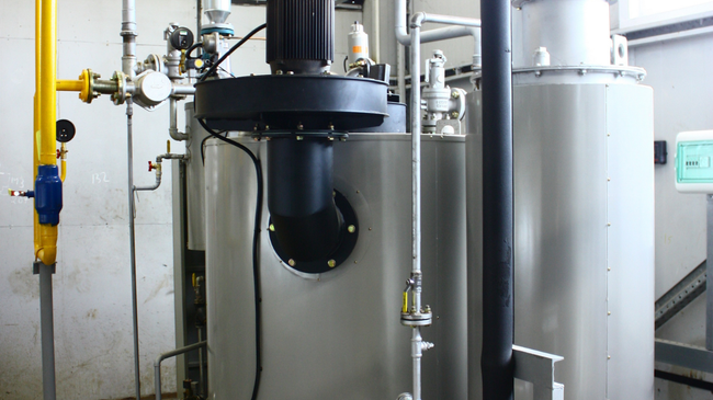Industrial pipes and tanks with a black pump unit in a mechanical room