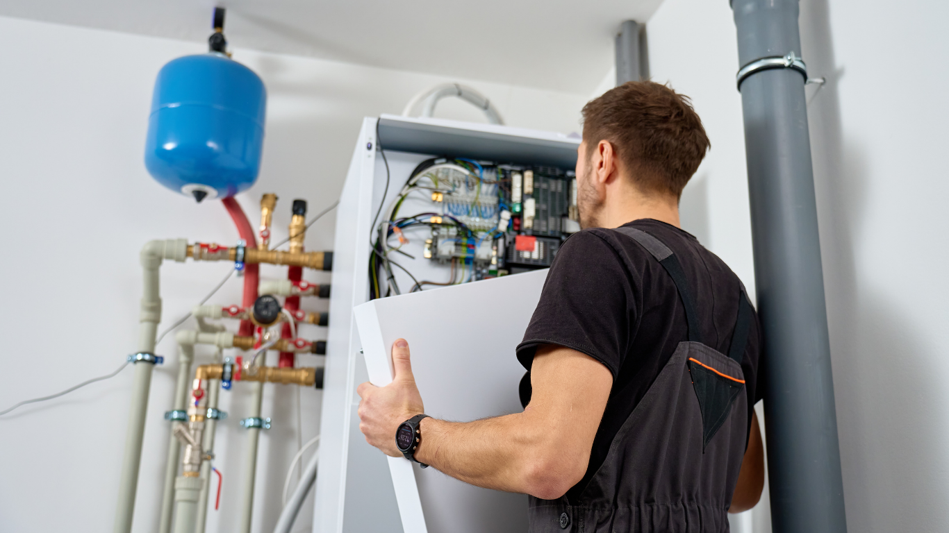Technician inspecting an open boiler system with pipes, wiring, and a blue expansion tank.