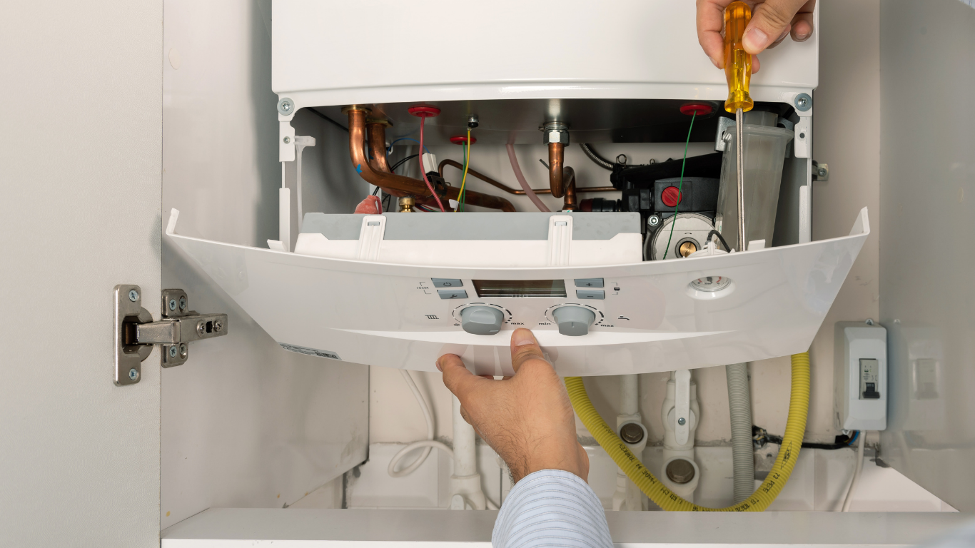 Technician repairing an open wall-mounted boiler with tools and exposed pipes
