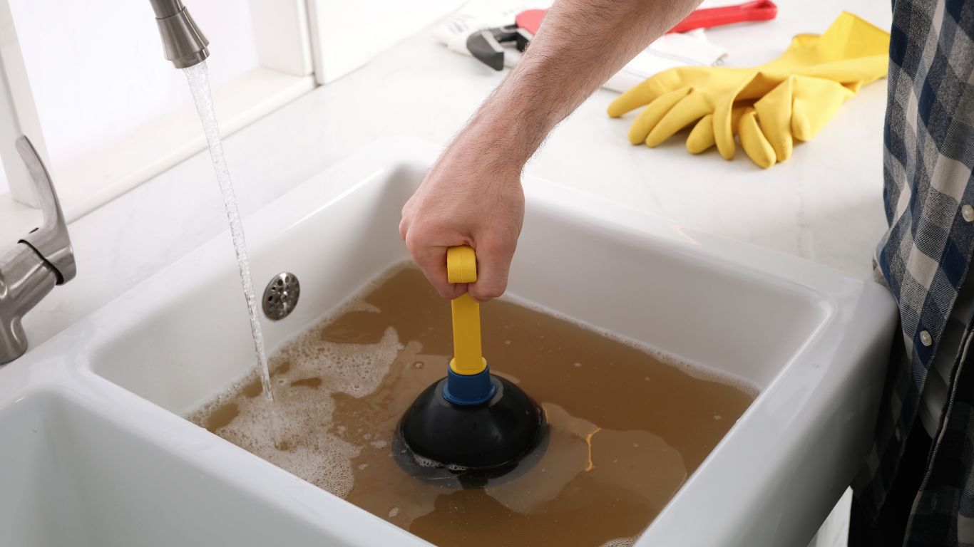 Person using a plunger in a sink full of muddy water, with a bunch of bananas nearby.