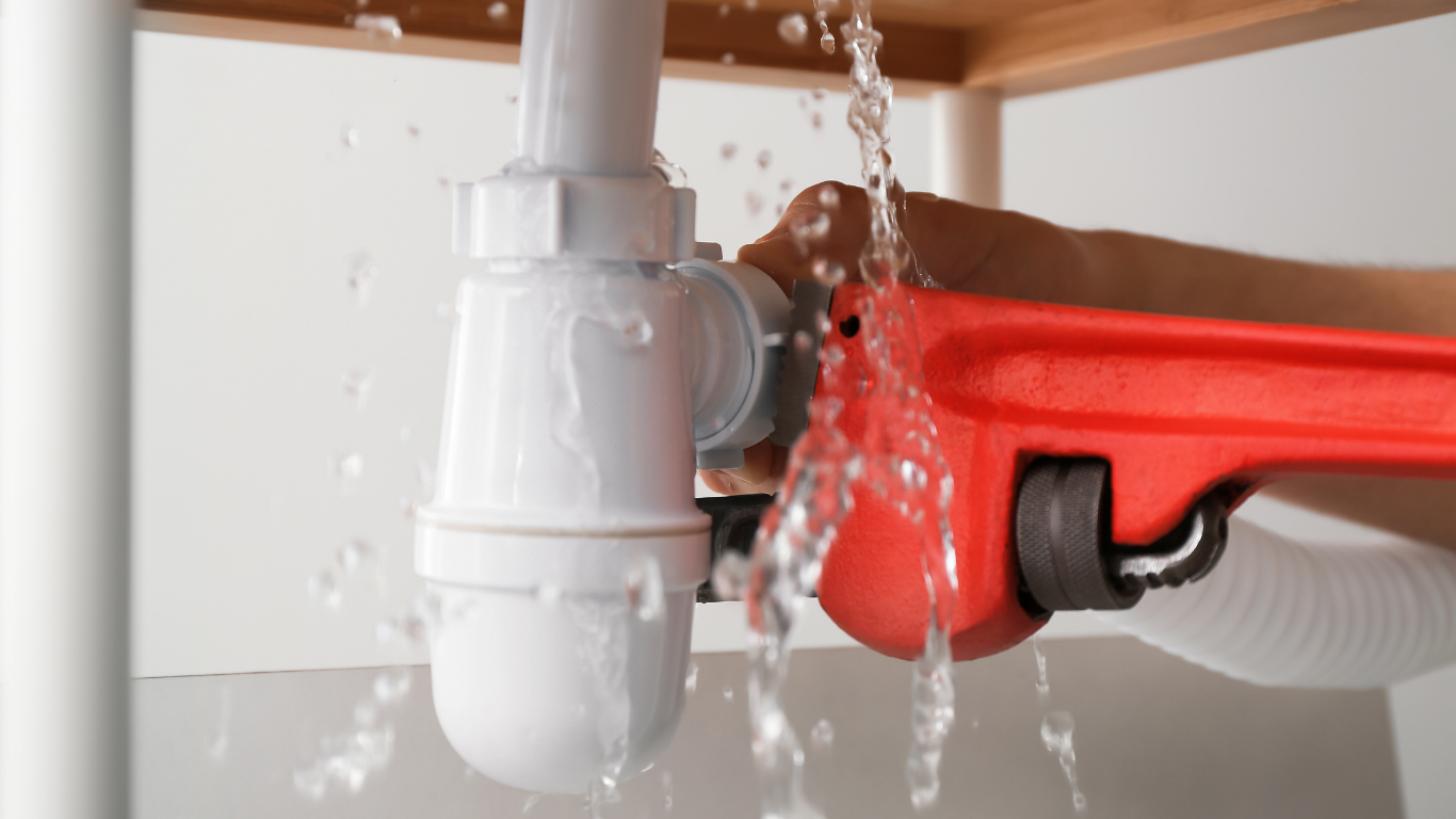 Water leaking from a white drain pipe under a sink, with a red clamp on the pipe.