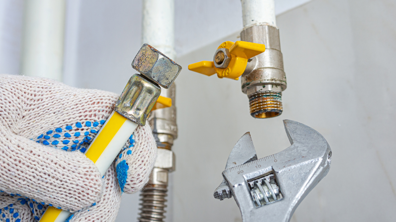 Gloved hand using a wrench to tighten a yellow gas line fitting on a pipe connection