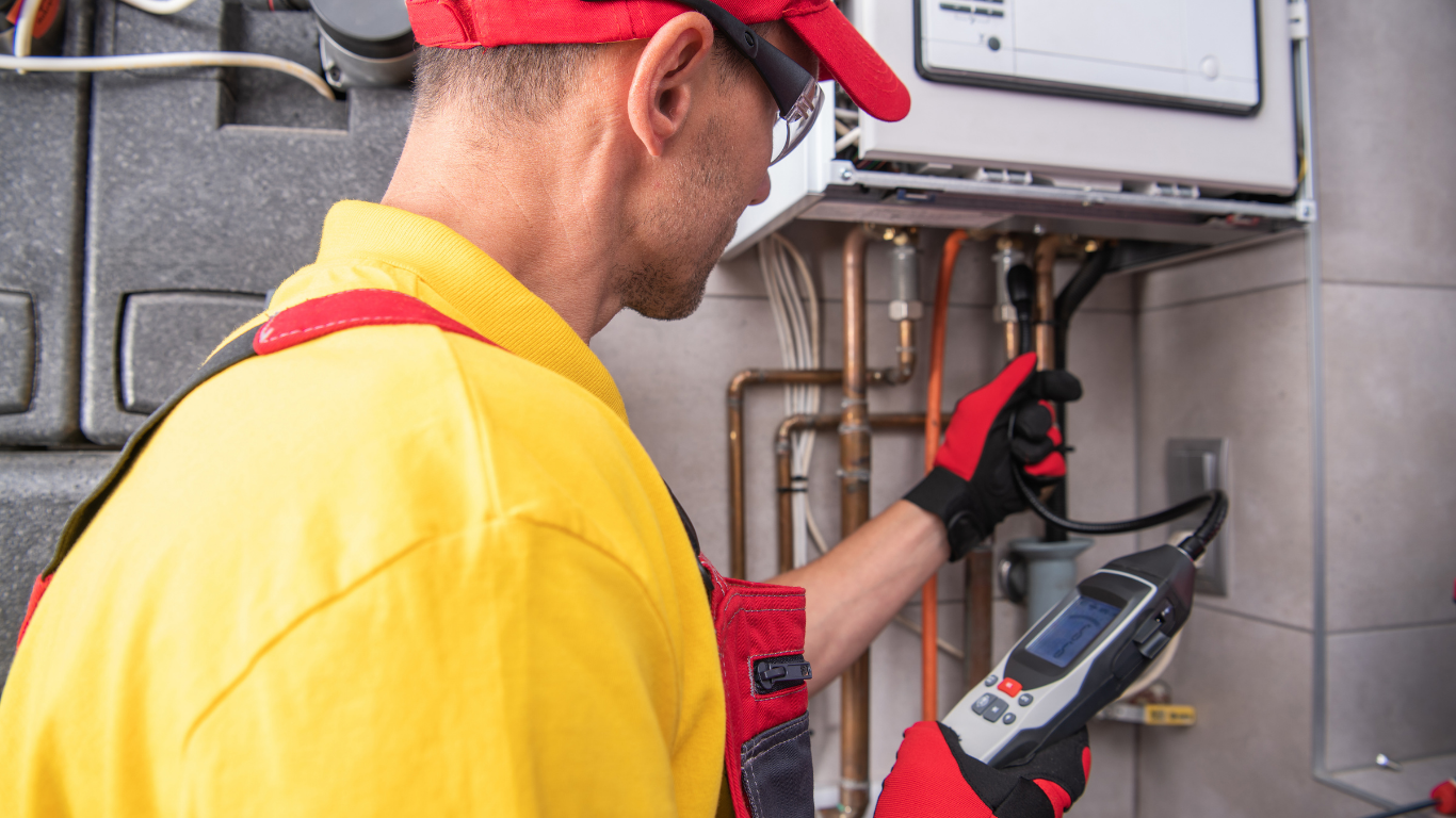 Technician in yellow shirt and red cap inspecting electrical panel with a multimeter.