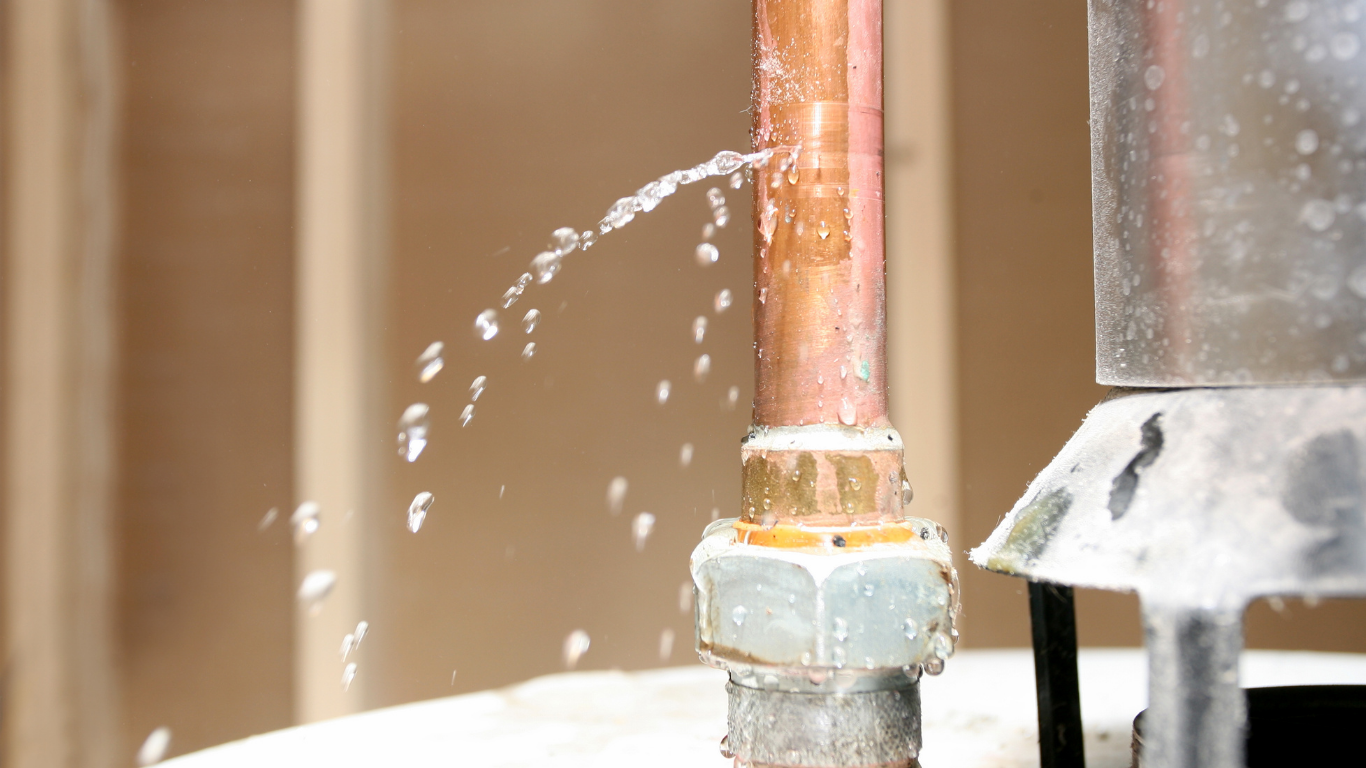 Copper pipe spraying water onto a white surface near a metal fitting