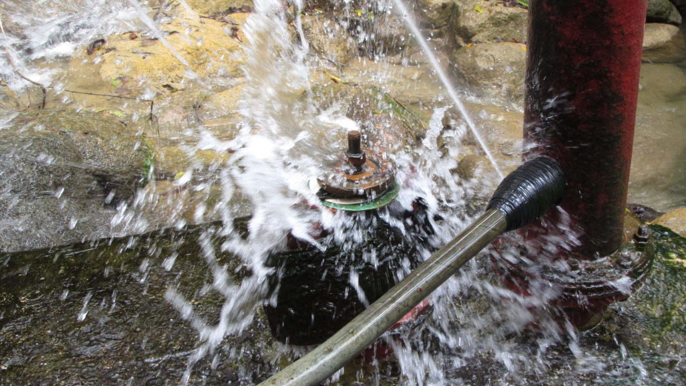 Water spraying from a pipe onto a green valve in a rocky stream.