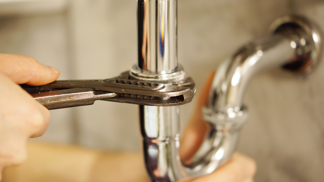 Hands using pliers to tighten a chrome pipe under a sink