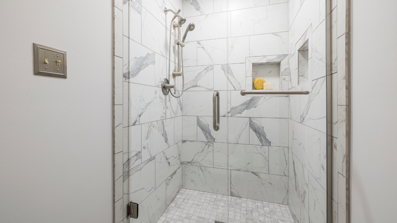 White tiled walk-in shower with glass door, grab bar, and showerhead in a bathroom.