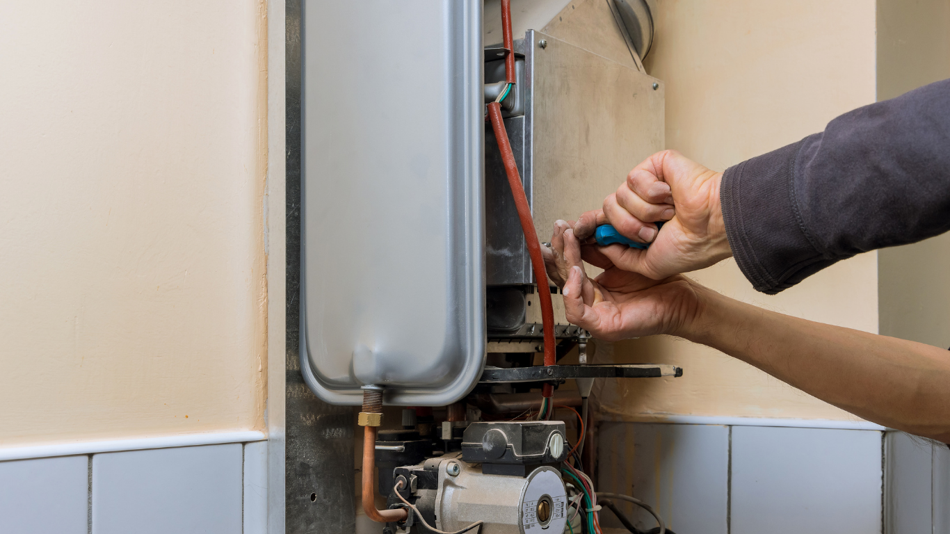 Technician adjusting a wall-mounted boiler with tools in a tiled utility room