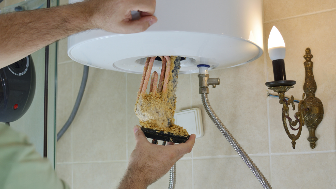 Hands servicing a wall-mounted water heater, with exposed pipes and a flexible hose in a tiled bathroom.