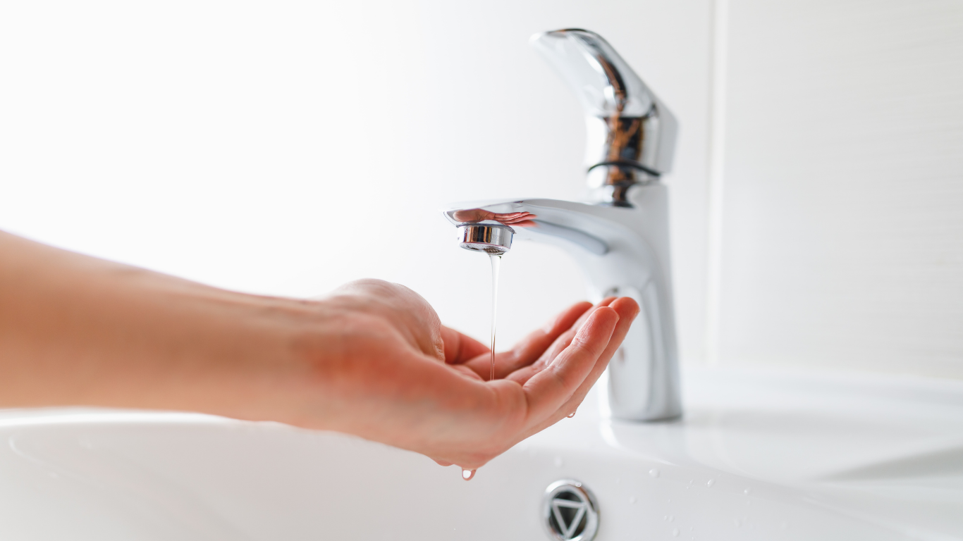 Hand under a chrome faucet catching running water in a white sink