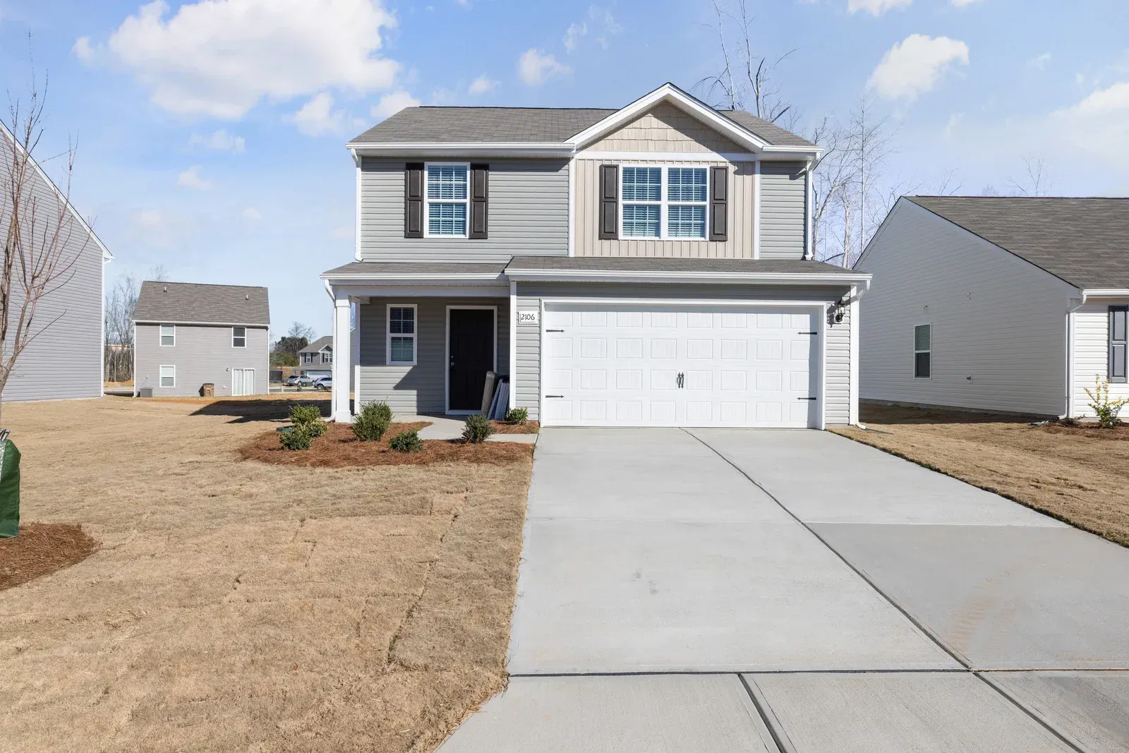 Two-story gray house with white garage door and driveway, against a sunny, blue sky.