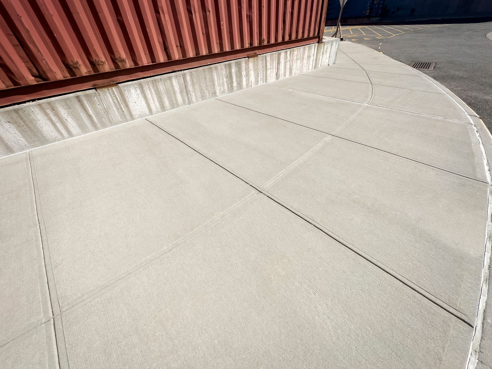 Curved concrete walkway next to a red industrial building. The walkway has evenly spaced, diagonal lines.