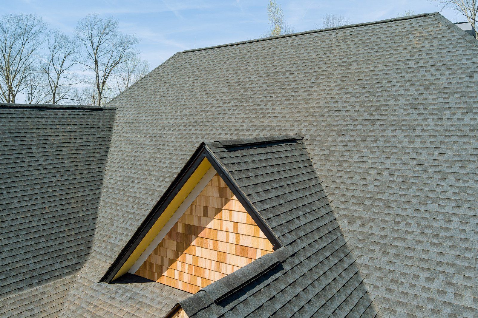 Gray asphalt shingle roof with a wooden accent, against a blue sky.