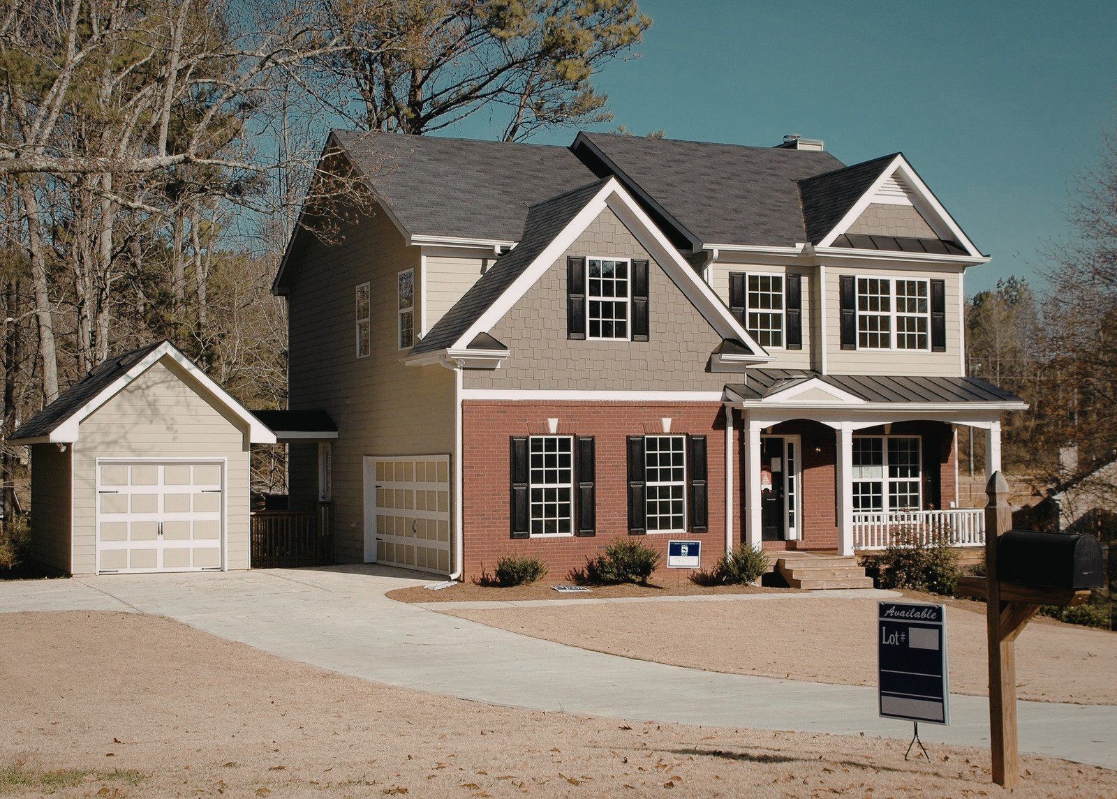 Two-story house with attached garage, tan siding, brick facade, black shutters, and a porch.
