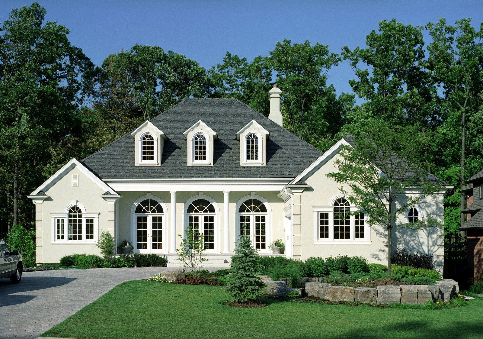 Beige house with gray roof, white trim, arched windows, and a green lawn.
