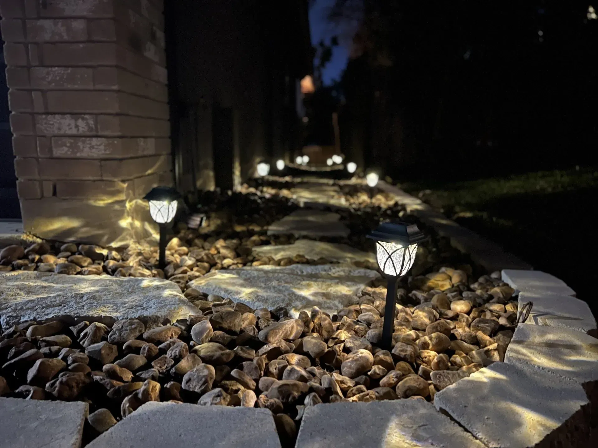 Pathway lit by solar lights at night. Stone path with surrounding rocks and a brick pillar.