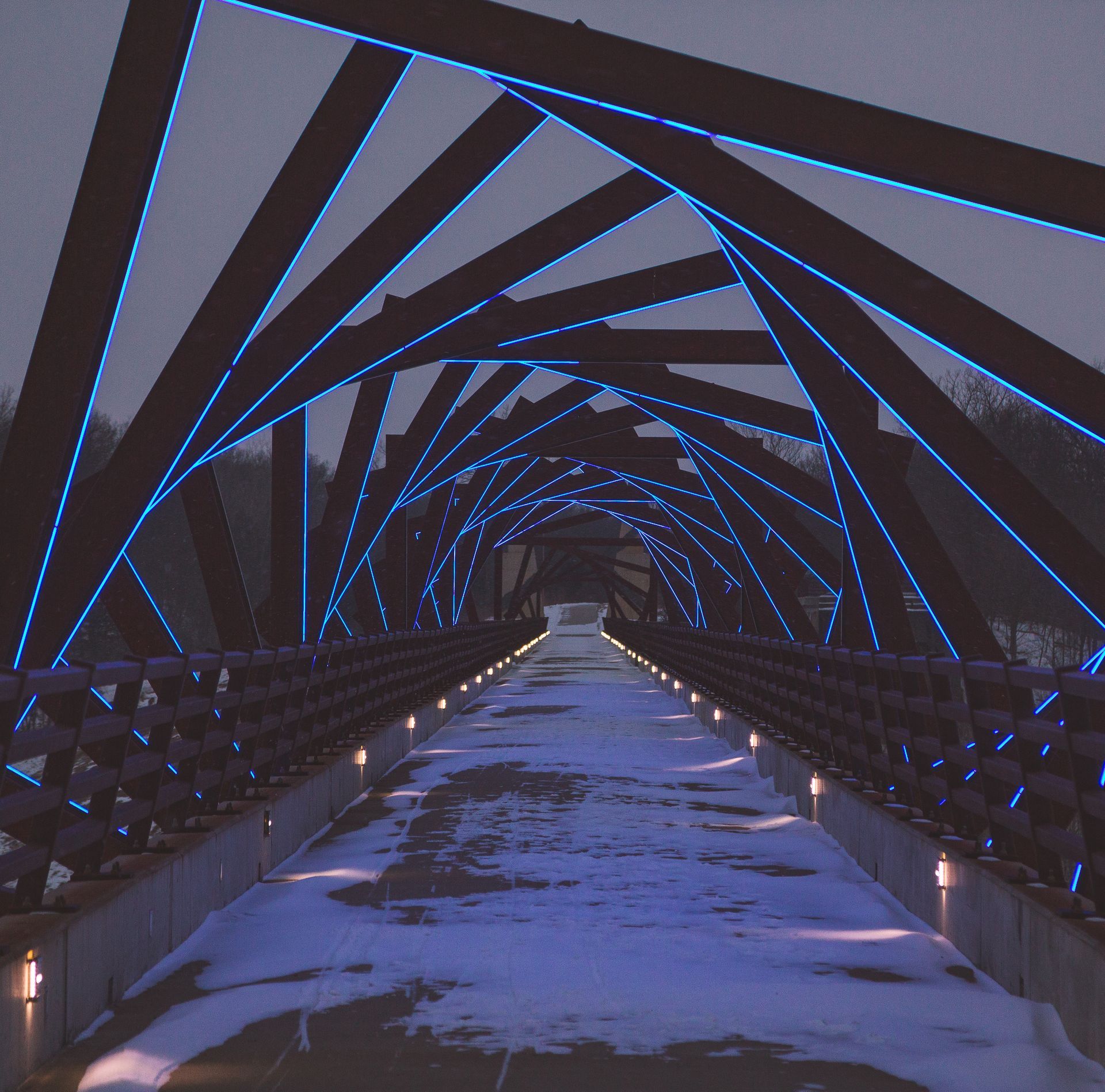Metal bridge with blue lights, snowy path, dusk setting.