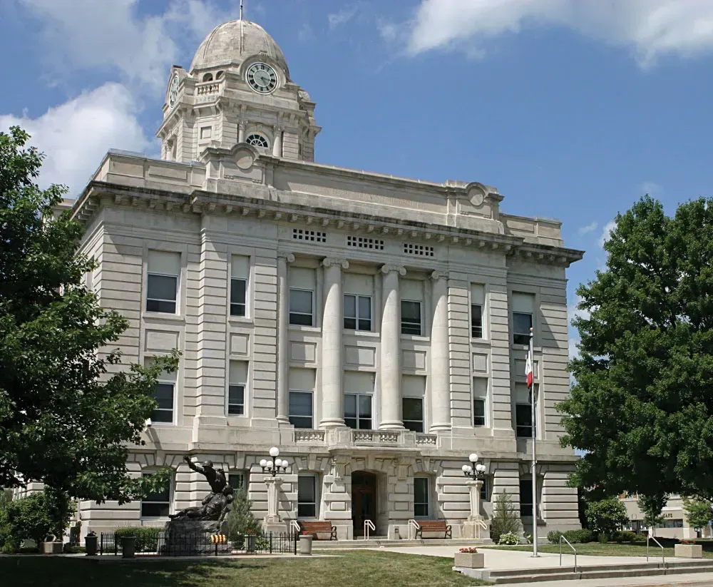 Gray stone courthouse with clock tower and trees.