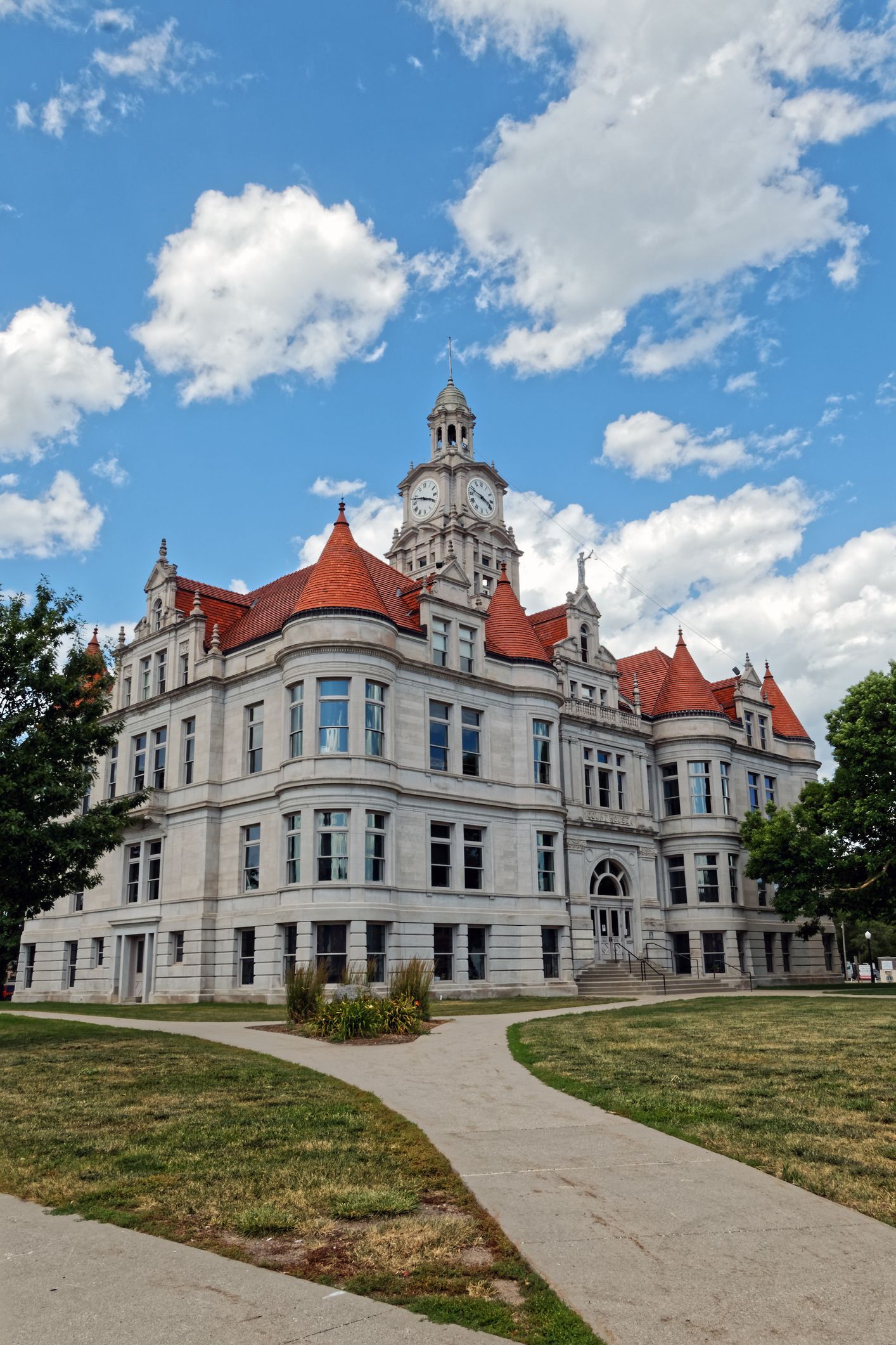 Historic courthouse with red roof, white facade, and clock tower, under a blue sky with clouds.