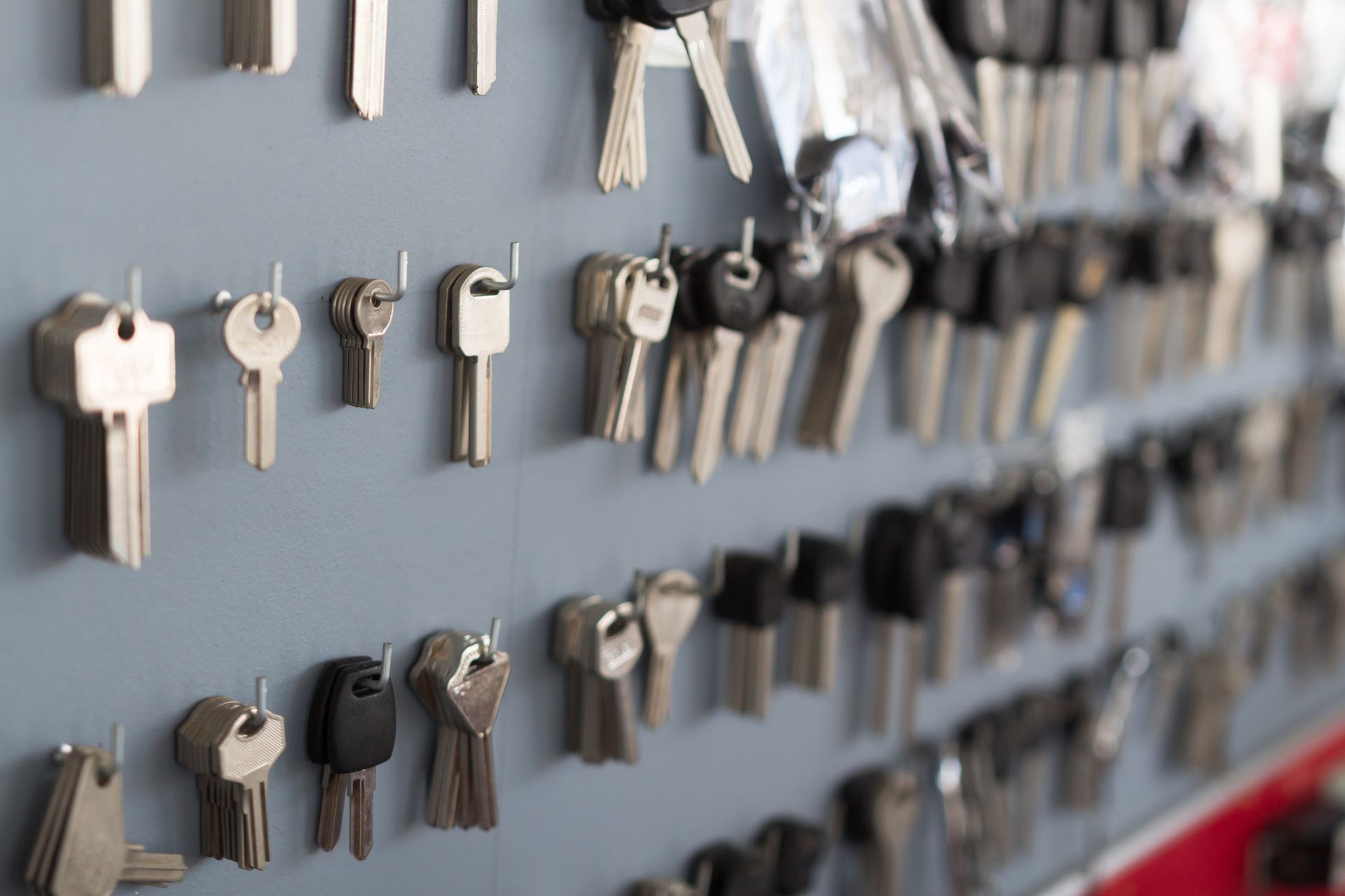 Keys hanging on a gray wall, likely at a locksmith shop. Various shapes and sizes.
