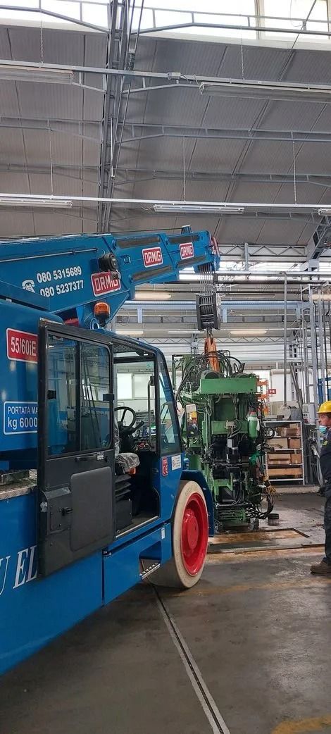Gru mobile blu in un capannone industriale con operai e attrezzature industriali nelle vicinanze.