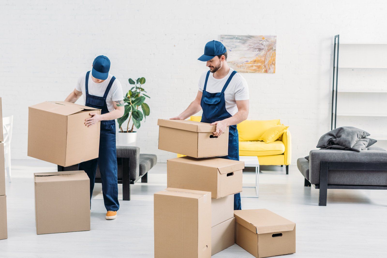 Professional movers in matching uniforms carefully transport cardboard boxes filled with belongings within a contemporary apartment.